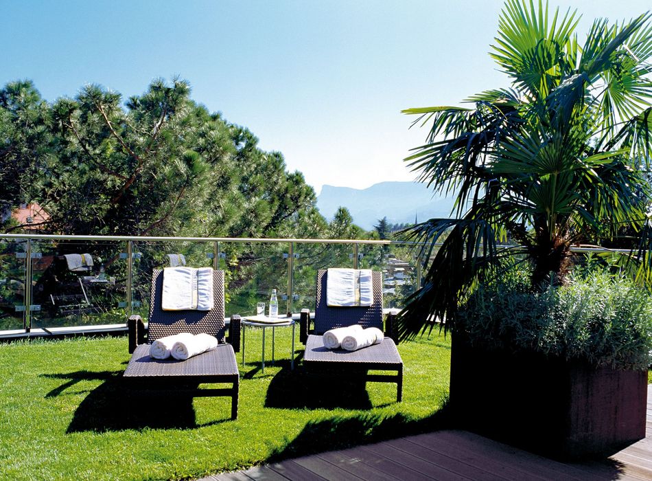 Two lounge chairs with towels on green grass terrace, glass railing, and palm tree under clear blue sky Two lounge chairs with towels on green grass terrace, glass railing, and palm tree under clear blue sky