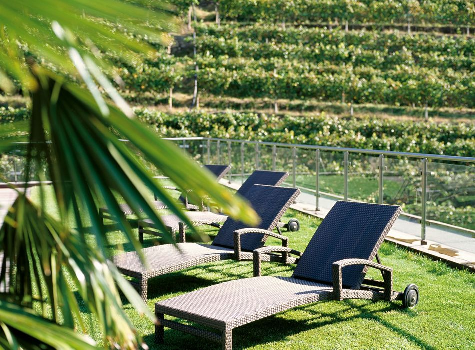 Wicker lounge chairs on a green lawn with a backdrop of vineyard terraces and a glass railing. Wicker lounge chairs on a green lawn with a backdrop of vineyard terraces and a glass railing.