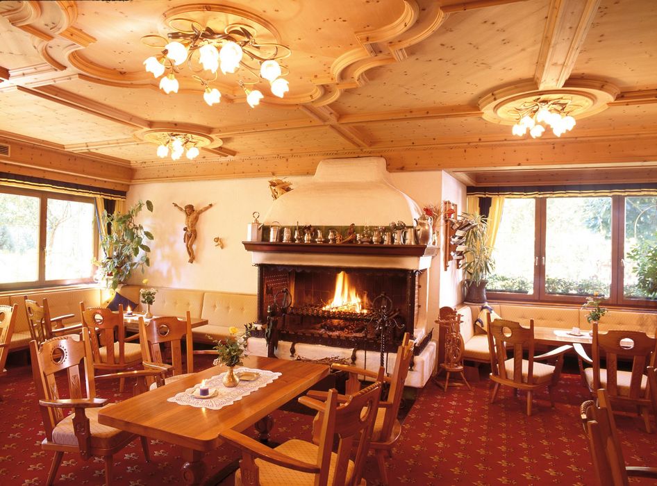 Cozy restaurant interior with wooden furniture, a lit fireplace, decorative ceiling, and large windows letting in natural light. Cozy restaurant interior with wooden furniture, a lit fireplace, decorative ceiling, and large windows letting in natural light.