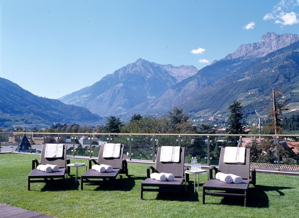 Four lounge chairs with towels on a grassy terrace overlooking mountains under a clear blue sky Four lounge chairs with towels on a grassy terrace overlooking mountains under a clear blue sky